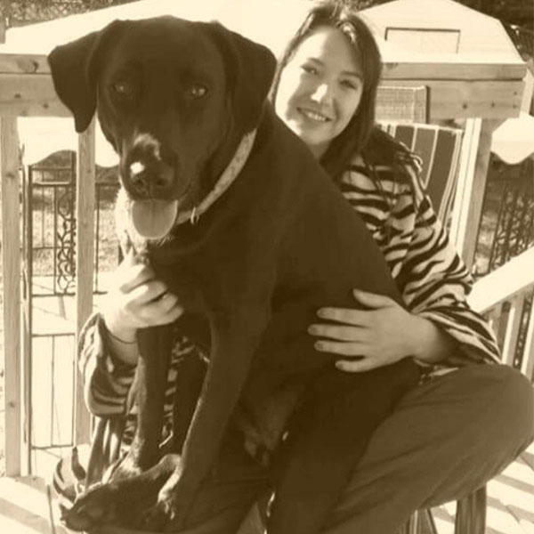 Nicole, dog bather, outside on a porch with large dog in her lap